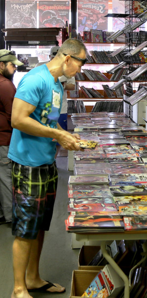 Customer in comic book store looking through stacks of comics.